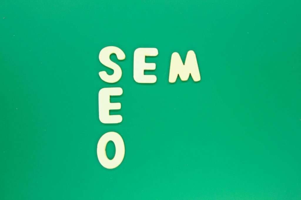 SEO Hannover - Das Bild zeigt Holzbuchstaben auf grünem Hintergrund, die vertikal die Wörter „SEO“ und horizontal „SEM“ bilden und den Buchstaben „S“ gemeinsam haben. Dadurch wird der Unterschied zwischen SEO und SEM auf kreative Weise optisch hervorgehoben. Local SEO Agentur Hannover.