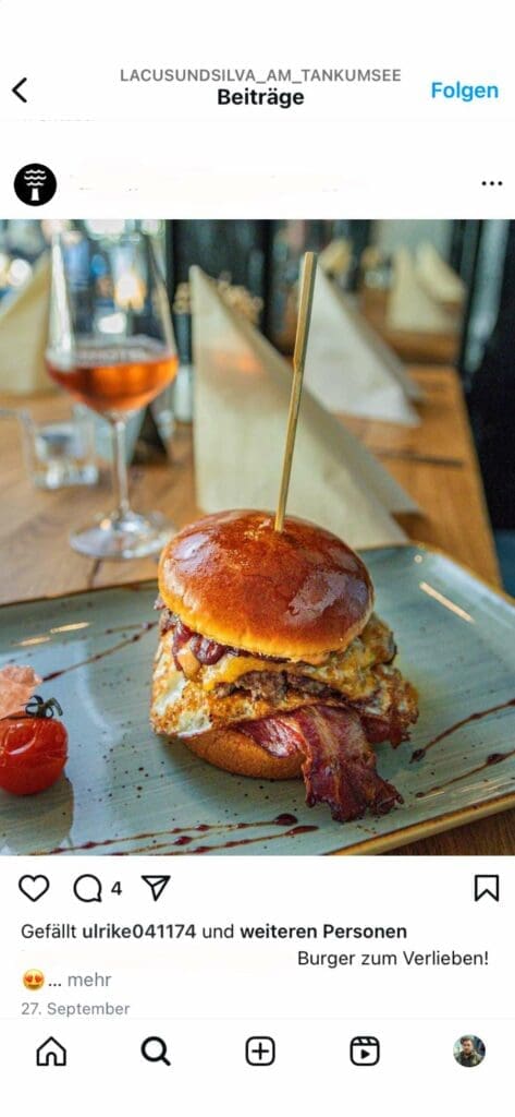 Webdesign Hannover - Ein Gourmet-Burger mit Speck, Käse und Soße ist auf einem Spieß auf einem rechteckigen Teller aufgespießt und fängt die Essenz der Food-Fotografie für einen Instagram-Feed ein. Daneben liegen eine Kirschtomate und ein Klecks Soße, perfekt harmonierend mit einem Glas Roséwein vor verschwommenem Tischgedeck im Hintergrund. Local SEO Agentur Hannover.