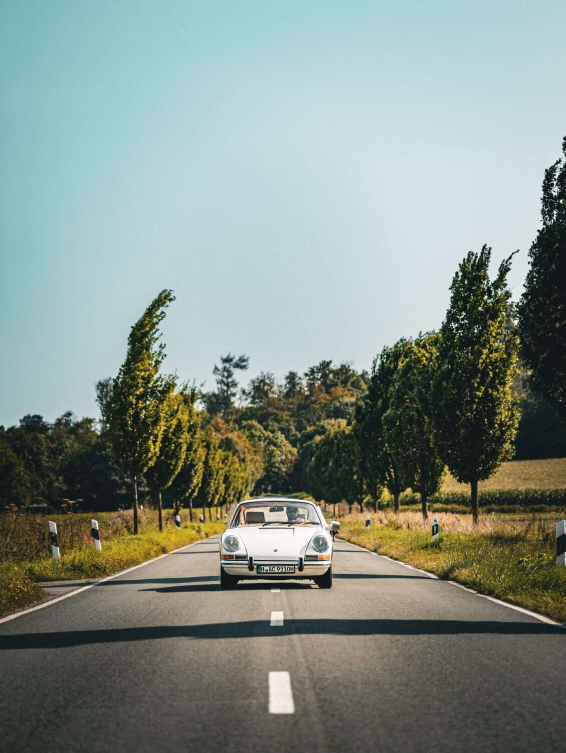 Webdesign Hannover - Ein weißer Oldtimer-Sportwagen gleitet eine zweispurige, von Bäumen gesäumte Landstraße entlang und wurde an einem sonnigen Tag unter einem klaren blauen Himmel in atemberaubenden Details fotografiert. Local SEO Agentur Hannover.