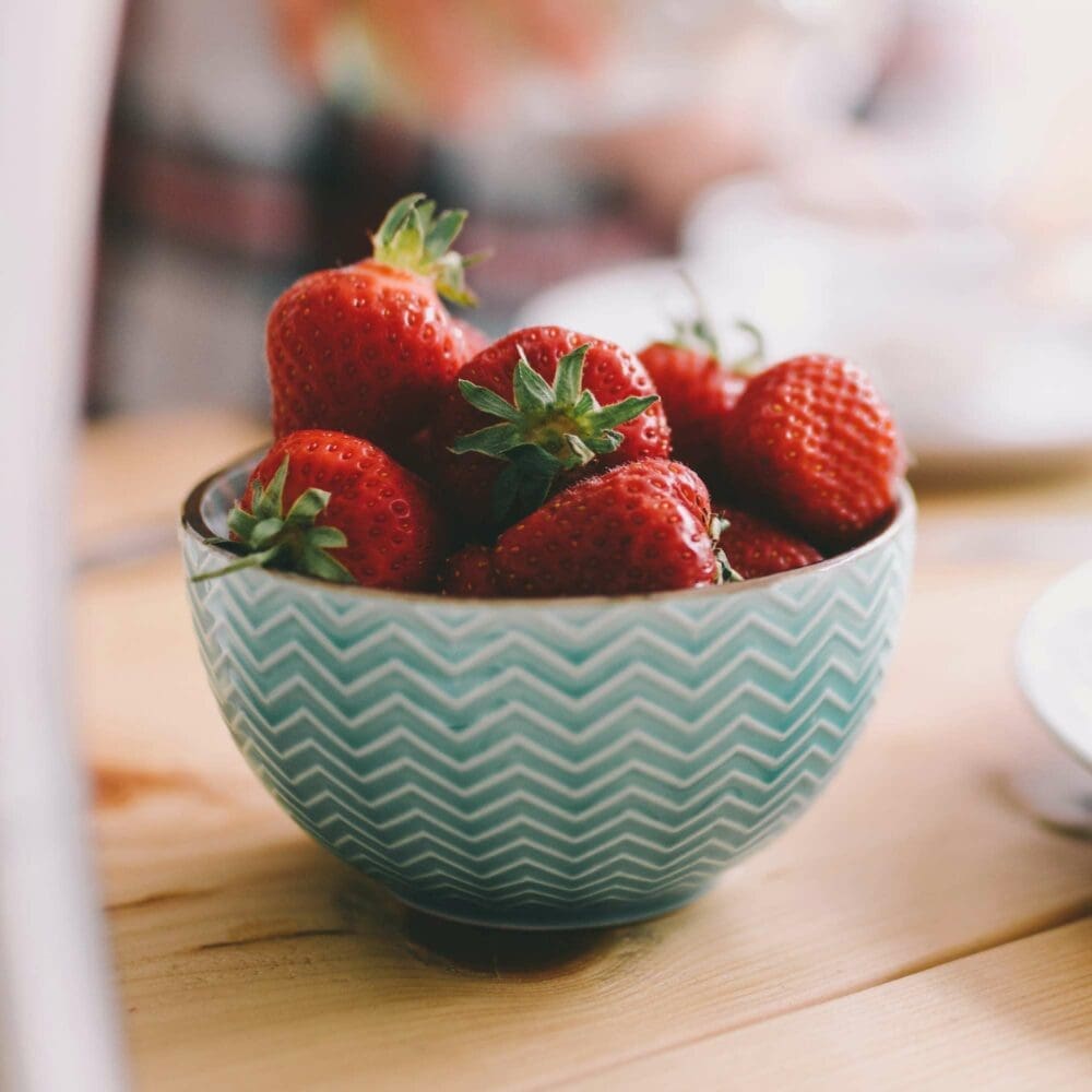SEO Hannover - Eine türkisfarbene Schale mit Zickzack-Muster ist mit frischen Erdbeeren gefüllt und fängt die Essenz der Food Fotografie gekonnt ein. Die Schale ruht auf einer Holzoberfläche, während der Hintergrund kunstvoll unscharf bleibt. Local SEO Agentur Hannover.