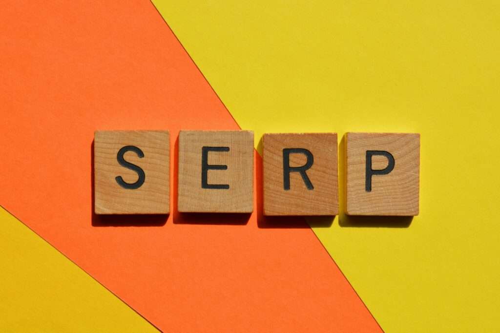 Webdesign Hannover - Holzfliesen bilden kunstvoll das Wort „SERP“ vor einem lebendigen Hintergrund, der geschickt diagonal zwischen Orange und Gelb aufgeteilt ist. Local SEO Agentur Hannover.