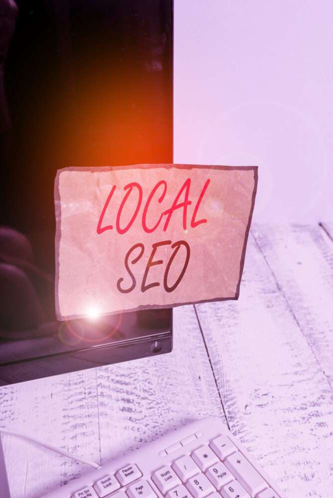 Webdesign Hannover - Ein Computermonitor mit einer handschriftlichen Notiz in roter und schwarzer Tinte mit der Aufschrift „Local SEO“, die auf den Bildschirm geklebt ist, auf einem weißen Holzschreibtisch mit einer teilweise sichtbaren Tastatur. Local SEO Agentur Hannover.
