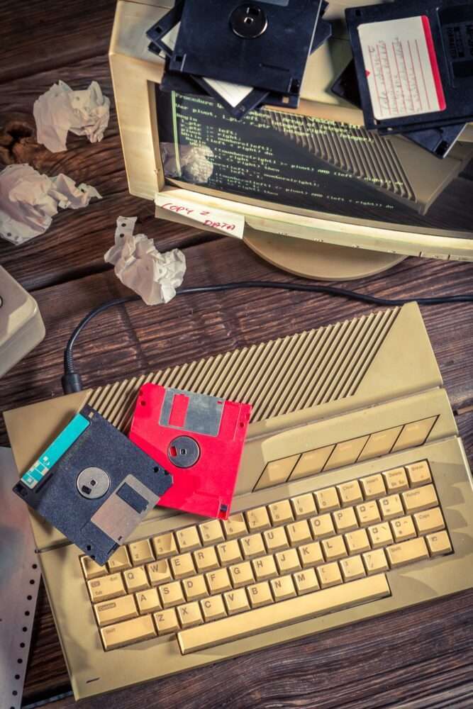 Webdesign Hannover - Ein Vintage-Computer mit einer beigen Tastatur, einem Monitor, auf dem Code angezeigt wird, und mehreren darauf verstreuten Disketten. Zerknüllte Papierkugeln deuten auf die Herausforderungen hin, die das Erstellen eines WordPress-Wartungsvertrags in dieser Retro-Computerumgebung mit sich bringt. Local SEO Agentur Hannover.