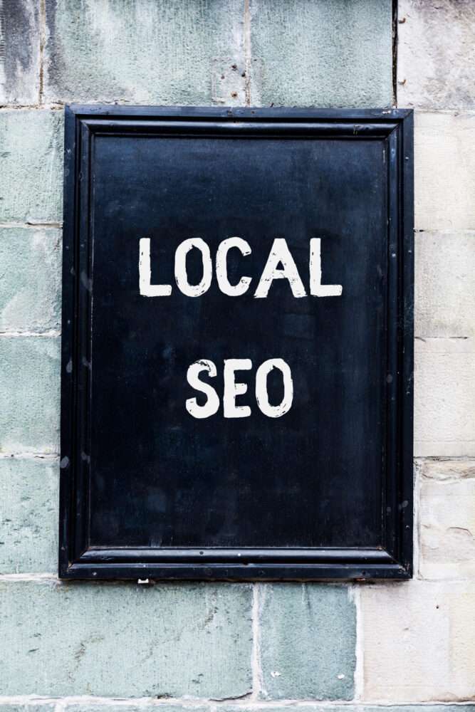 Webdesign Hannover - Ein schwarzes rechteckiges Schild an einer strukturierten Wand zeigt in fetten weißen Buchstaben die Worte „LOCAL SEO“. Die Hintergrundwand hat ein verwittertes Aussehen mit unterschiedlichen Grau- und Weißtönen. Local SEO Agentur Hannover.